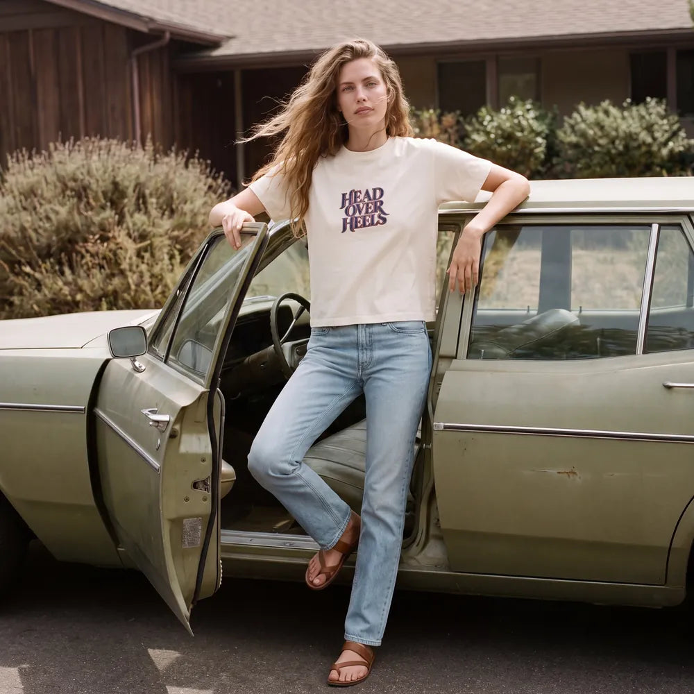 Woman stepping out of a vintage olive green car in a cream cropped tee printed HEAD OVER HEELS