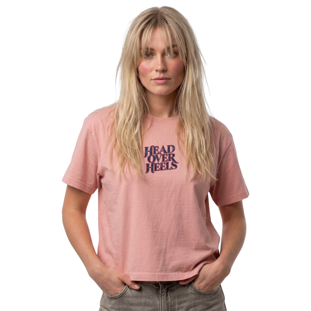 Woman wearing the dusty pink Course America boxy tee with HEAD OVER HEELS lettering across the chest