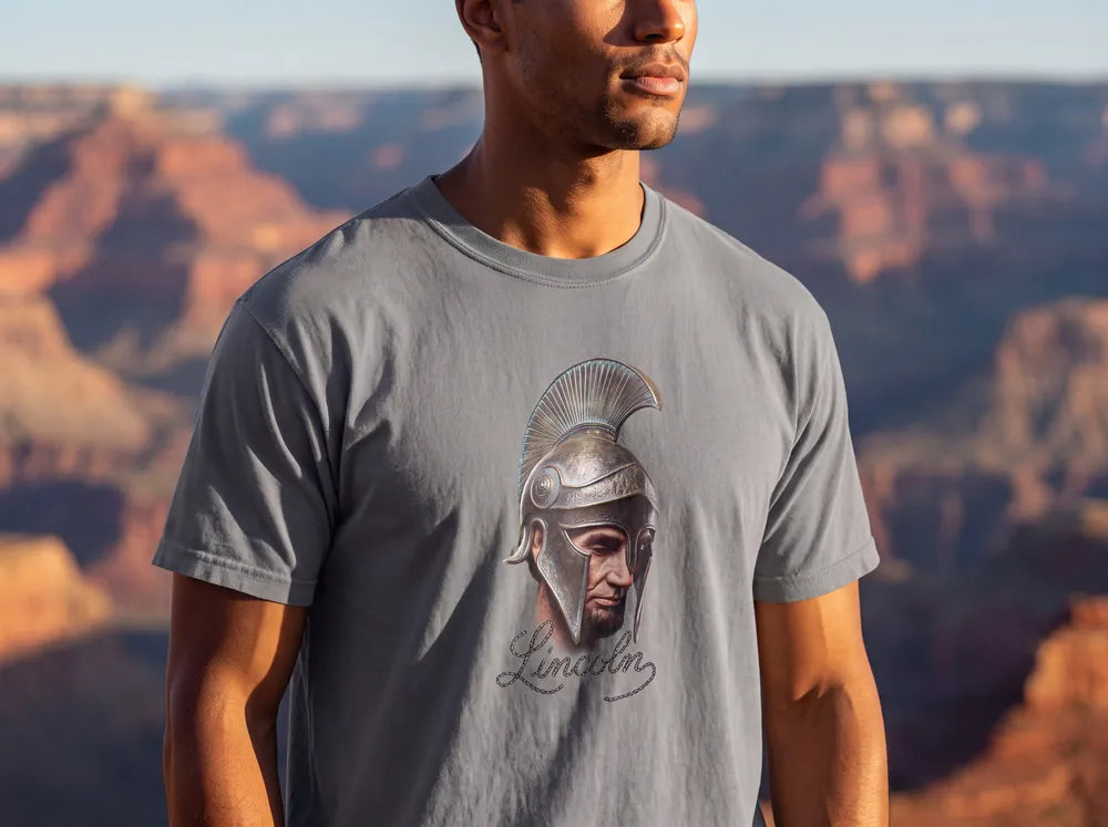 Man at a canyon overlook in a grey tee printed with Abraham Lincoln in a crested helmet above the word Lincoln in script