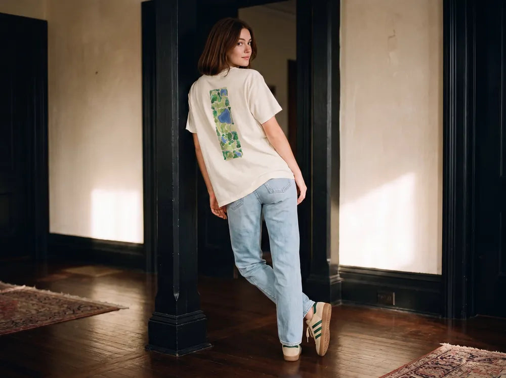 Woman in a wood floored room seen from behind in a cream boxy tee, the back print a watercolour map of Central Park